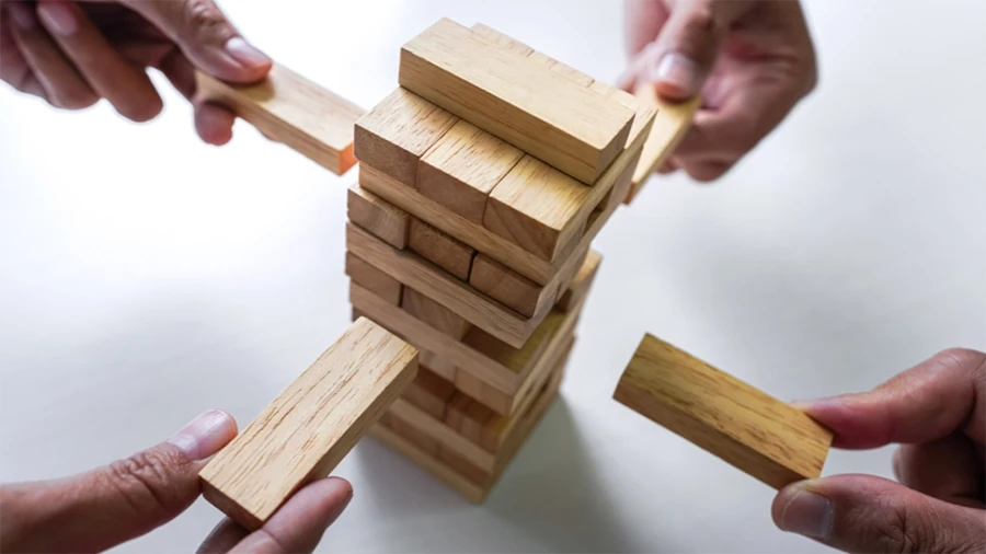 Close-up of several hands playing a wooden block stacking game, symbolizing teamwork, risk management, and strategic decision-making.