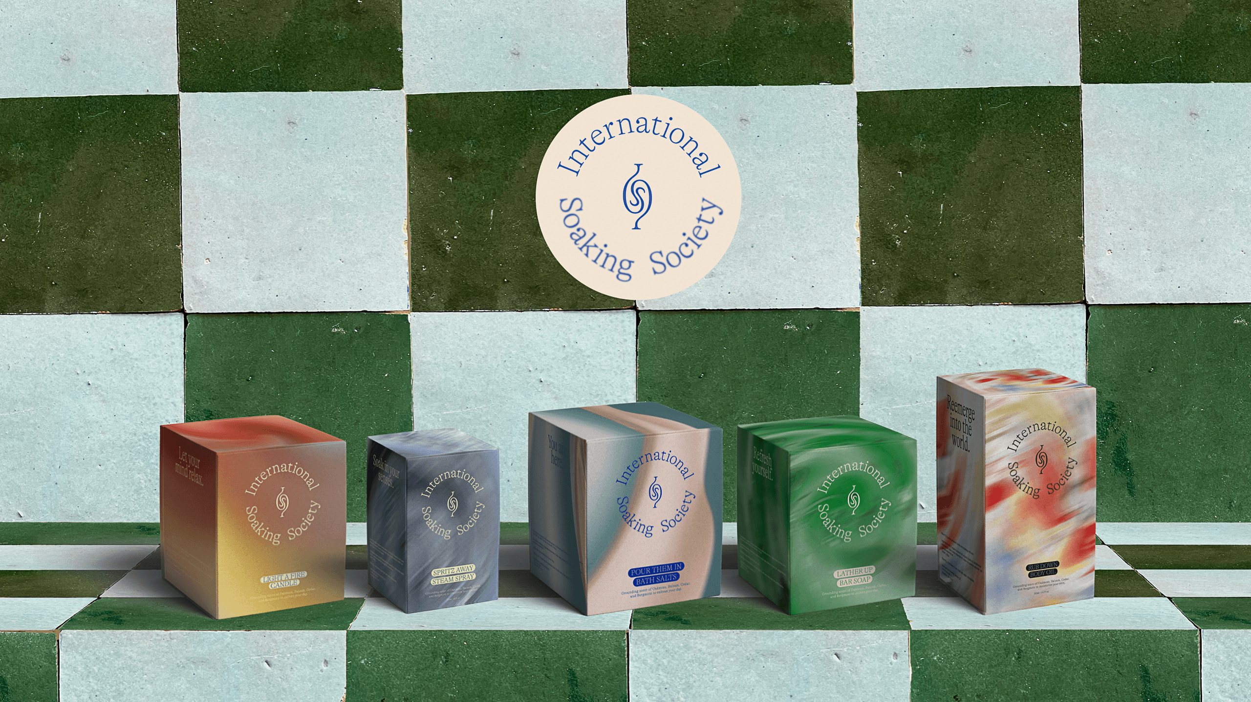 Five rectangular boxes of soap are arranged on a green and white checkered surface. The boxes vary in color and design, including shades of orange, gray, green, and white. Each box features the text "International Soaking Society" and a small logo. The boxes are positioned in a row, with the green and white checkered background providing a contrasting backdrop.