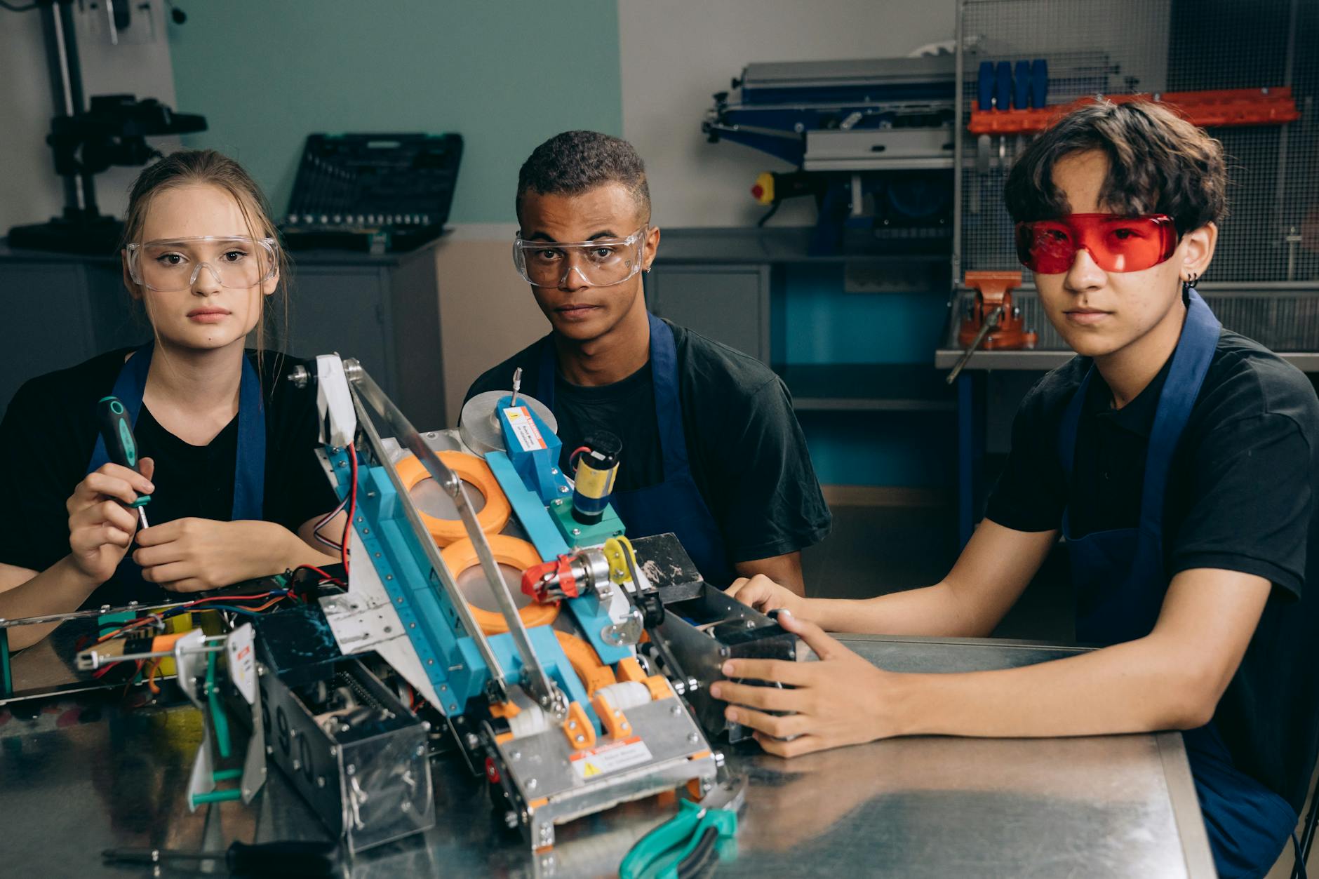 High school students collaborating on a robotics project with wires and a laptop at a science lab station.