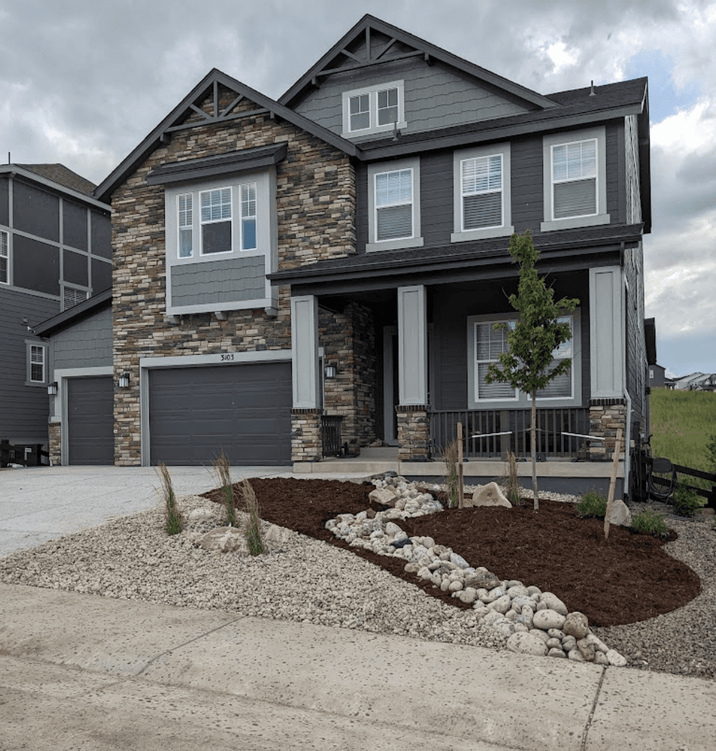 xeriscaping landscaping includes native grasses near the front door area and a small rocky garden bed next to the garage