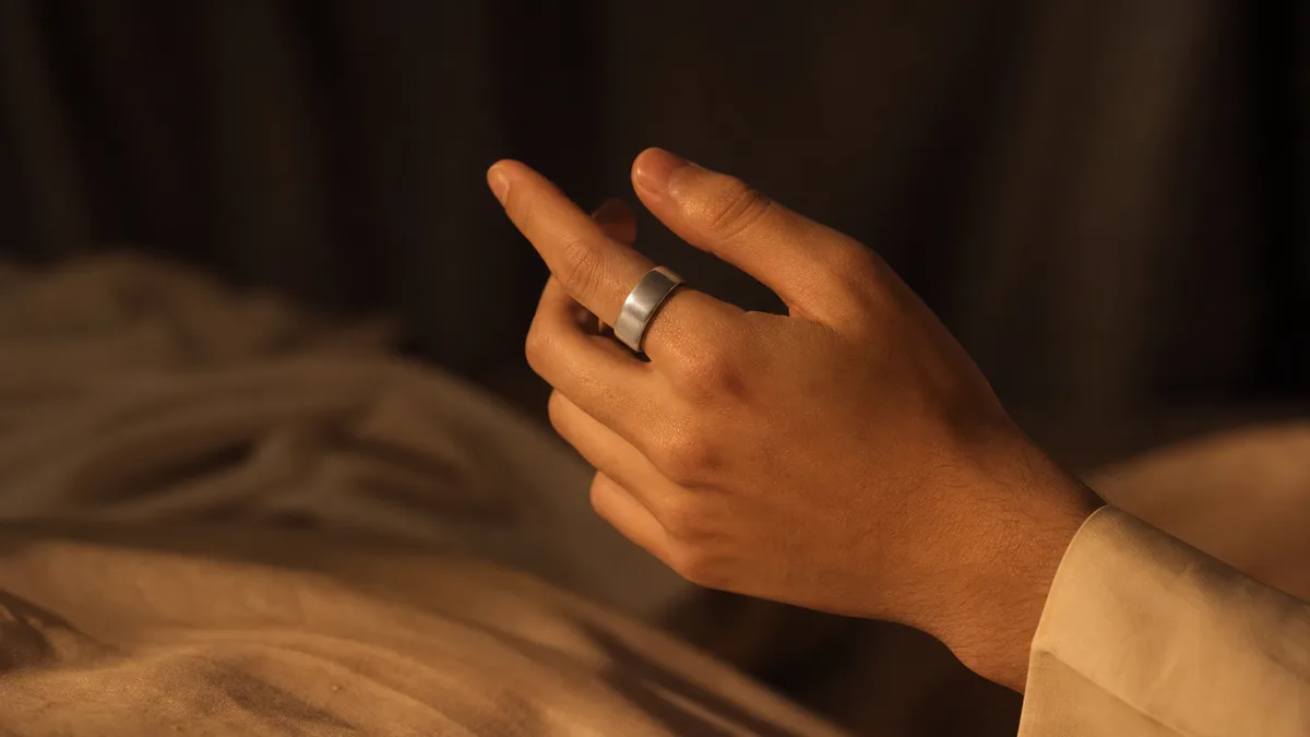 Hand wearing a plain silver smart tasbih ring in warm Ramadan lamplight