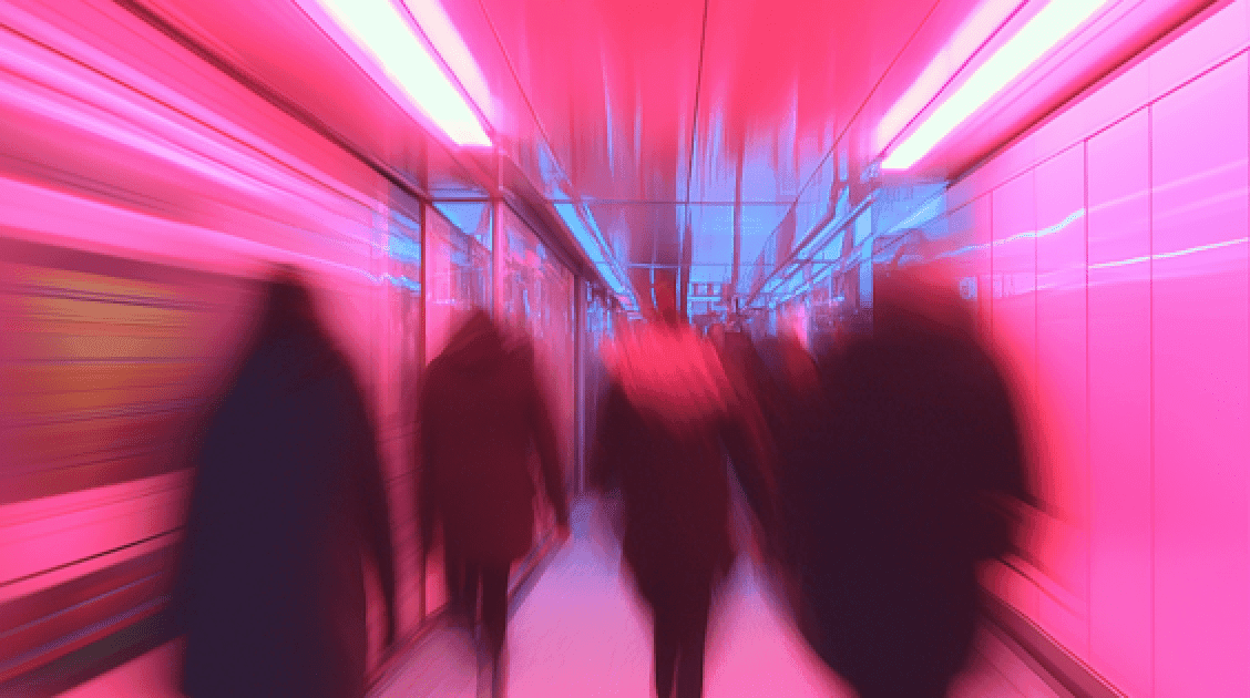 People walking through a subway tunnel illuminated by vibrant pink lights.