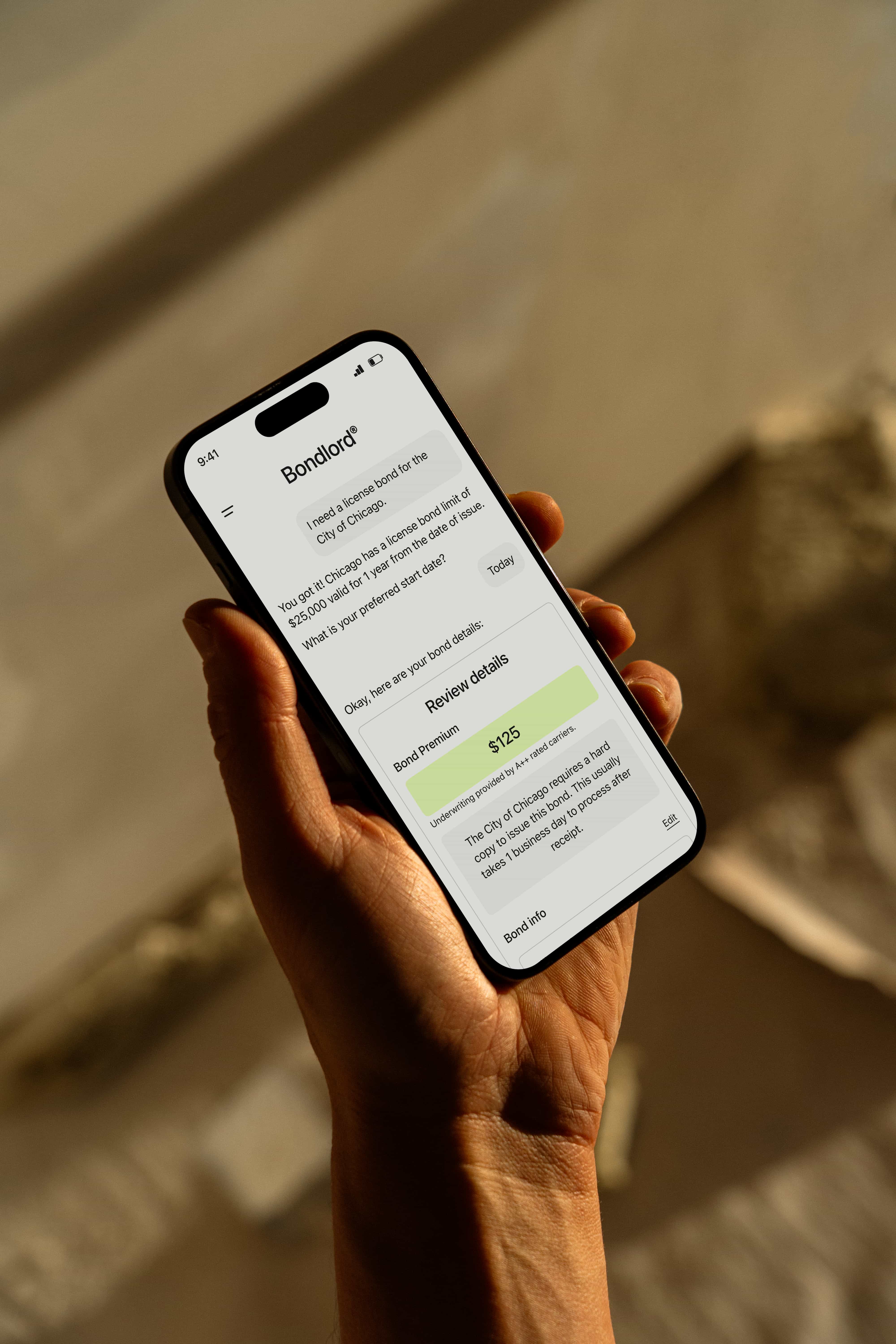 Hand holding a smartphone displaying the Bondlord app, where an AI chat helps a contractor request and review a license bond for the City of Chicago, including bond details and premium.