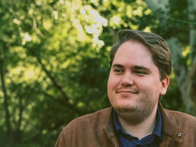 Alex smiles in a brown suede jacket