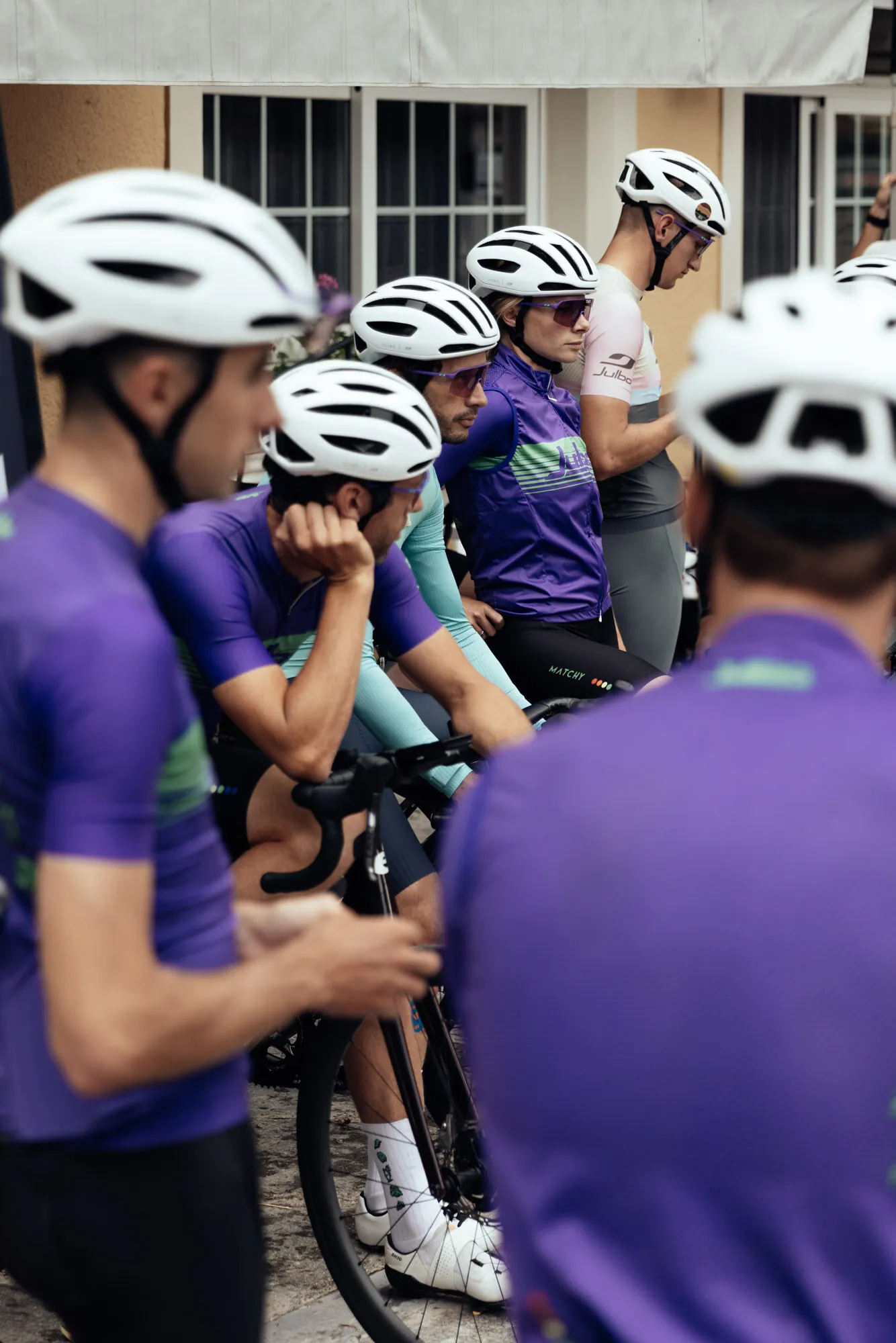 Groupe de cyclistes Julbo attentifs avant le départ, en maillots violets et casques blancs.