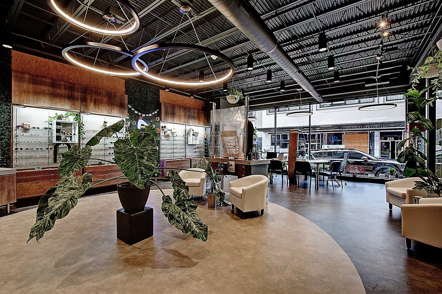 Modern interior space featuring a large plant, circular wooden tables, and contemporary seating. Warm lighting ambiance.