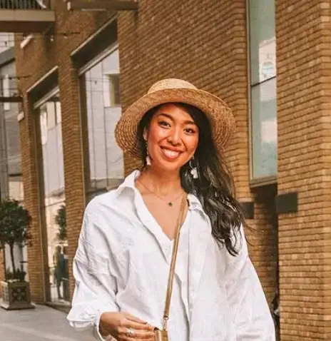 A woman with a hat standing in front of a brick building smiing
