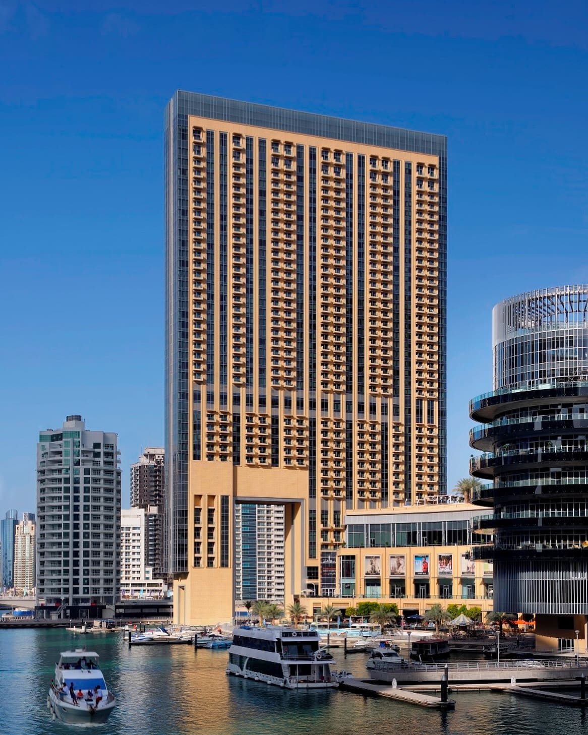 A tall residential tower in Dubai Marina with a grid of balconies and a modern facade against a clear, blue sky.