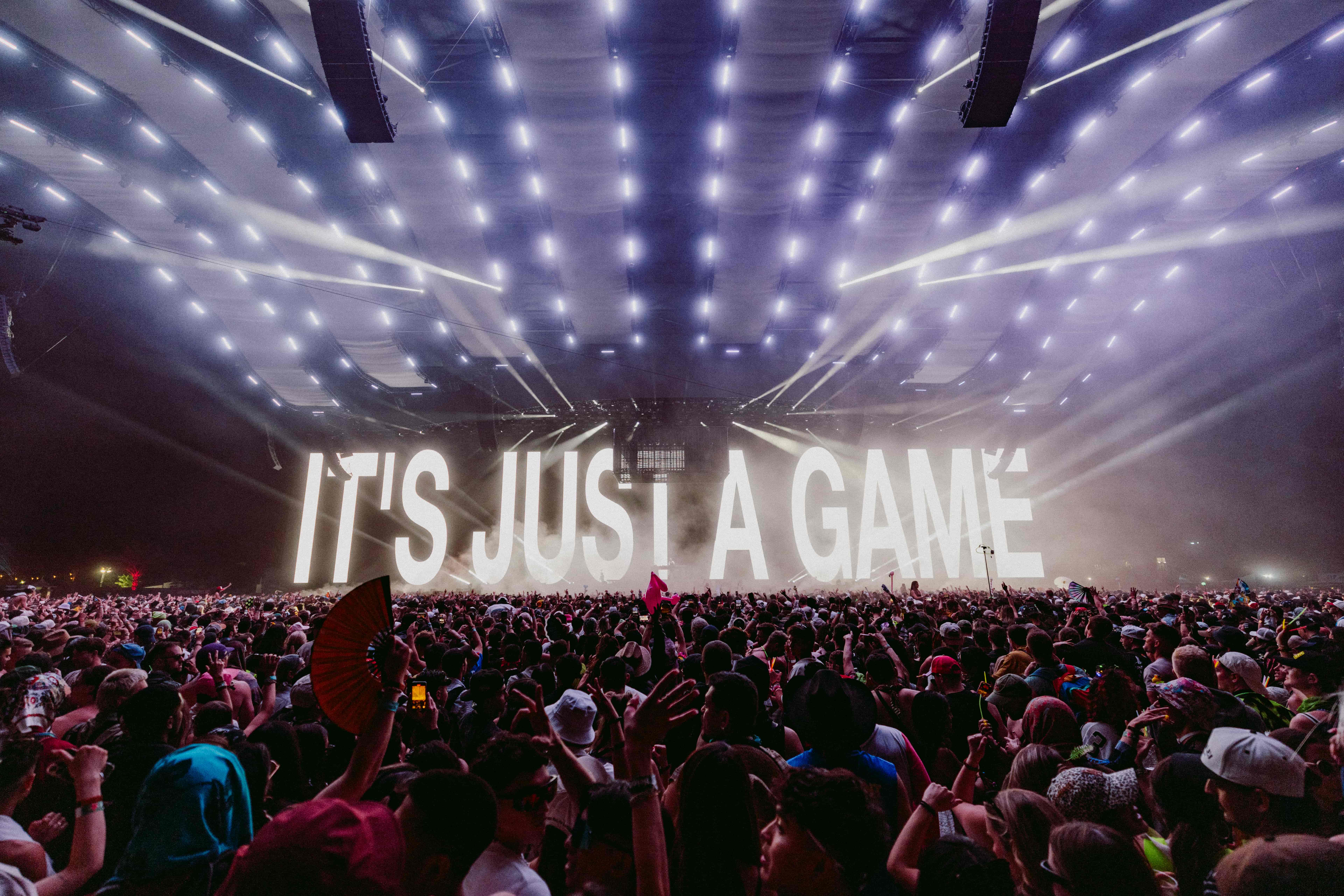 Wide crowd shot at Coachella 2025 with massive stage text reading “IT’S JUST A GAME” during MAU P’s performance, captured by A World Away creative director Brandon Densley