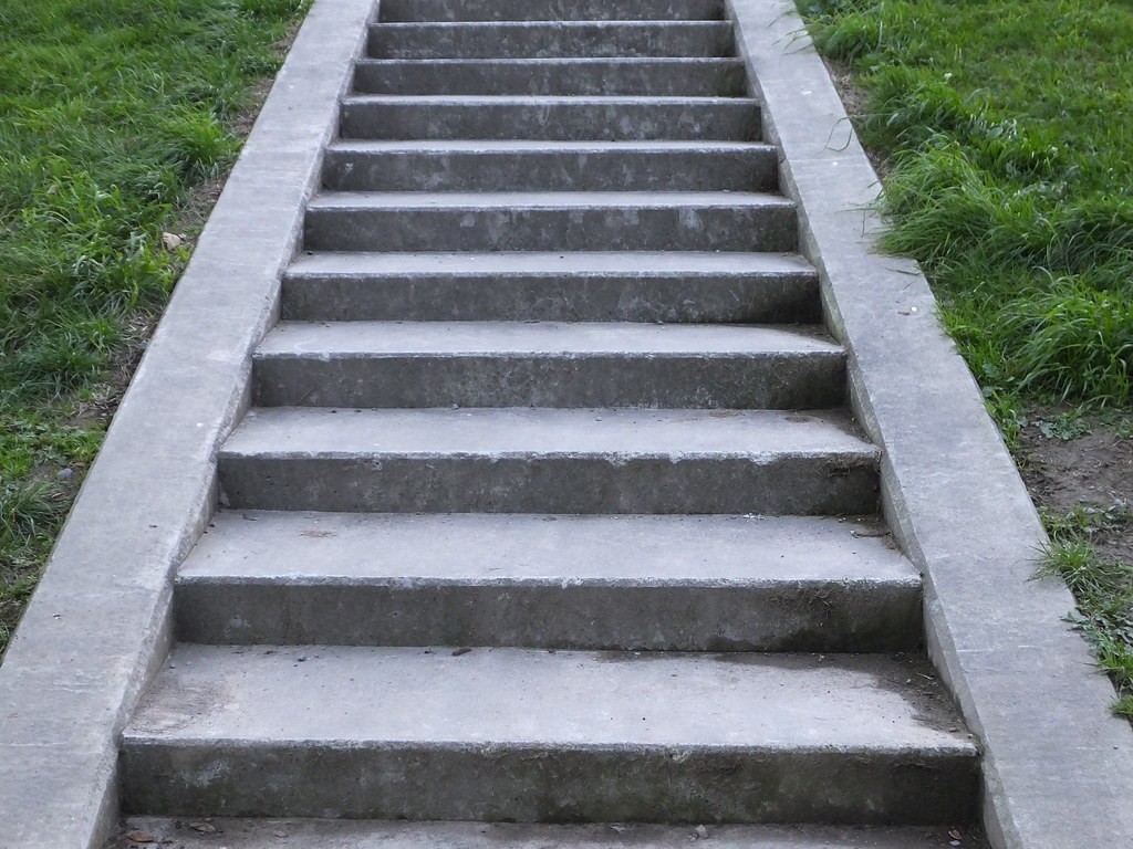 A series of concrete stairs leading upwards, surrounded by green grass on either side.