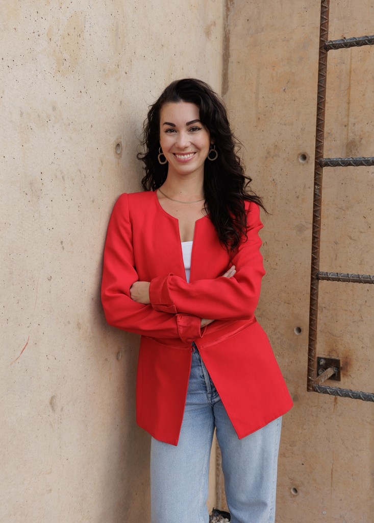 Close-up portrait of a person wearing a gray insulated hooded jacket with the hood up, showing their face framed by the hood against a light background.