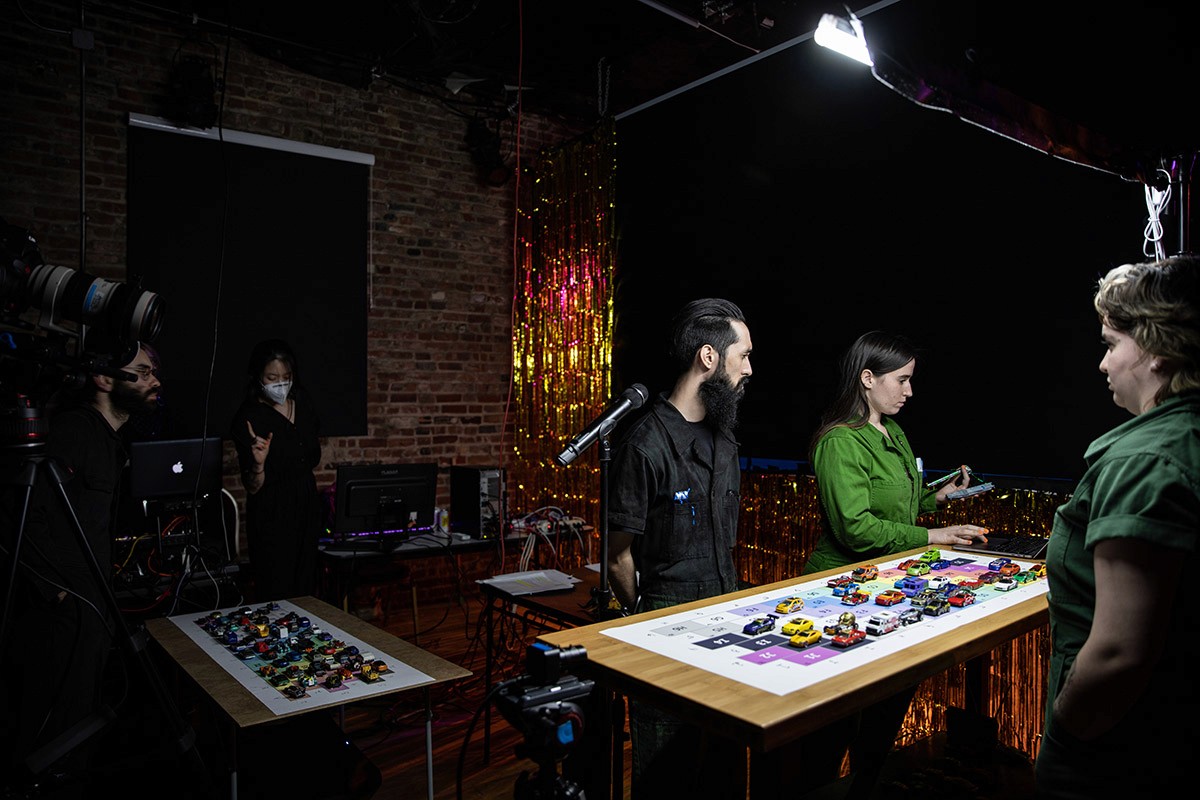 Three performers backstage with two production staff in the background.