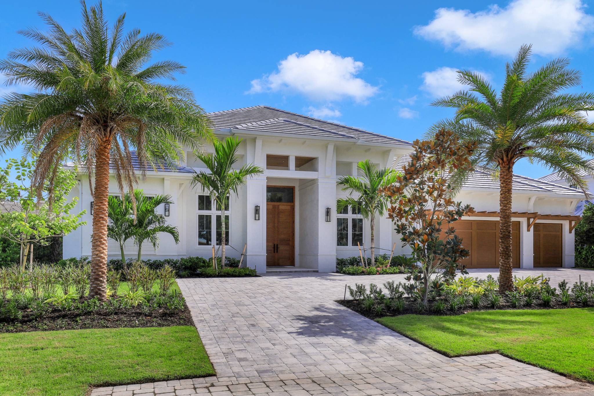 a british-indies styled entrance to a luxrious home with a paver driveway and palm trees lining the property