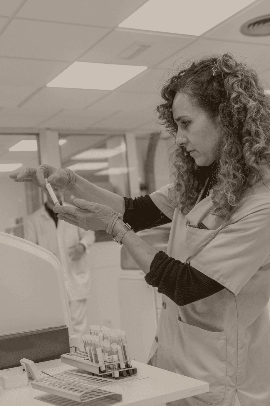 Scientist wearing safety goggles and blue lab attire, using a pipette to transfer liquid into a vial in a laboratory setting.