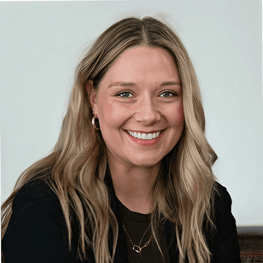 Smiling man with light brown hair and stubble, wearing a khaki shirt in natural light
