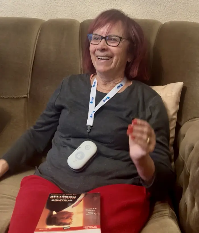 Una mujer sonríe sentada en el sofá, con la Lupa Inteligente colgada al cuello y un libro sobre las piernas