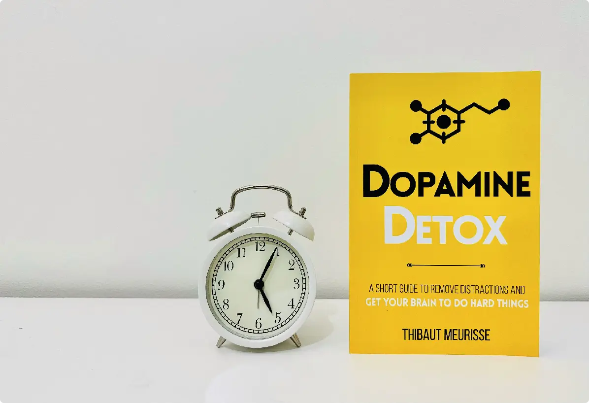 A small clock sits next to a bright yellow book titled "Dopamine Detox."