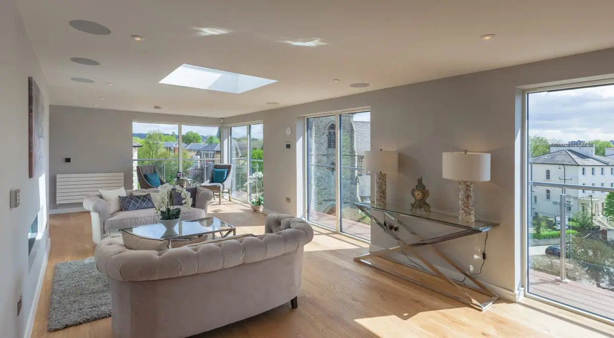 Modern minimalist house with large glass windows and a flat roof, surrounded by lush greenery. A serene pool reflects the trees and the sky. Peaceful ambiance.