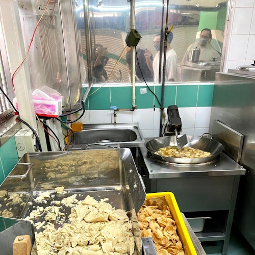 A commercial kitchen with dough and pasta being prepared. People are seen through a glass window in the background.