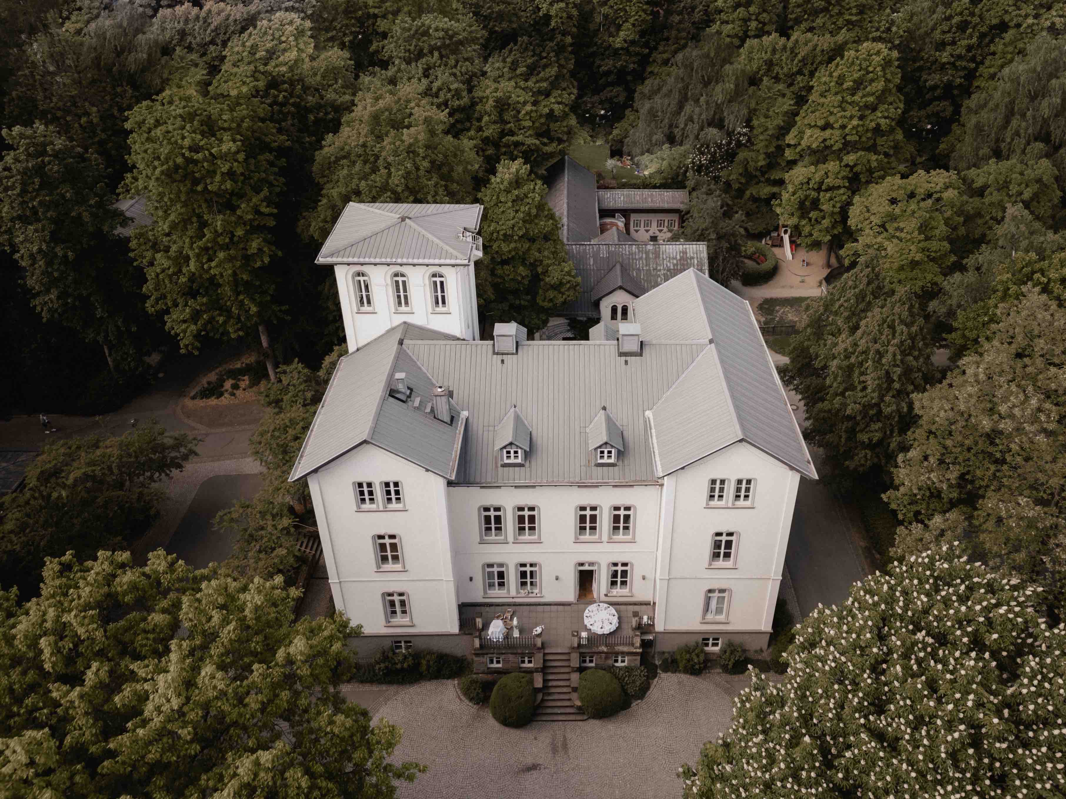 Weiße Villa Kreuztal mit grauem Dach, umgeben von Bäumen, aus der Vogelperspektive