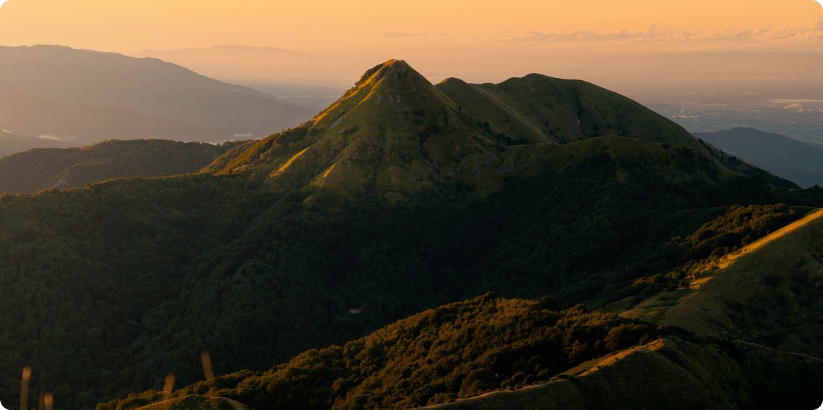 Mountain peak during sunset with lush green landscape and warm orange sky.
