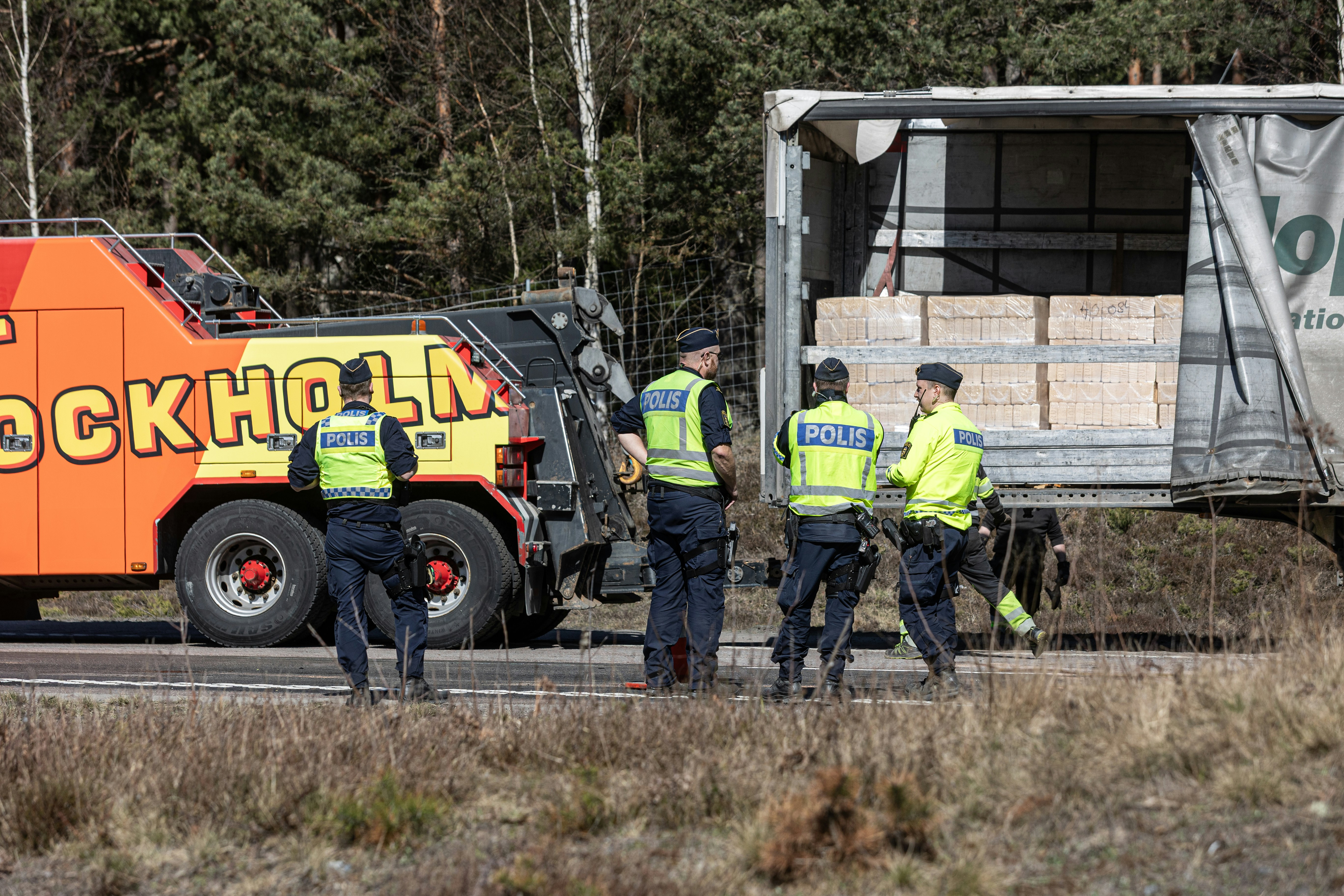 Police officers investigate a truck with a tow truck.