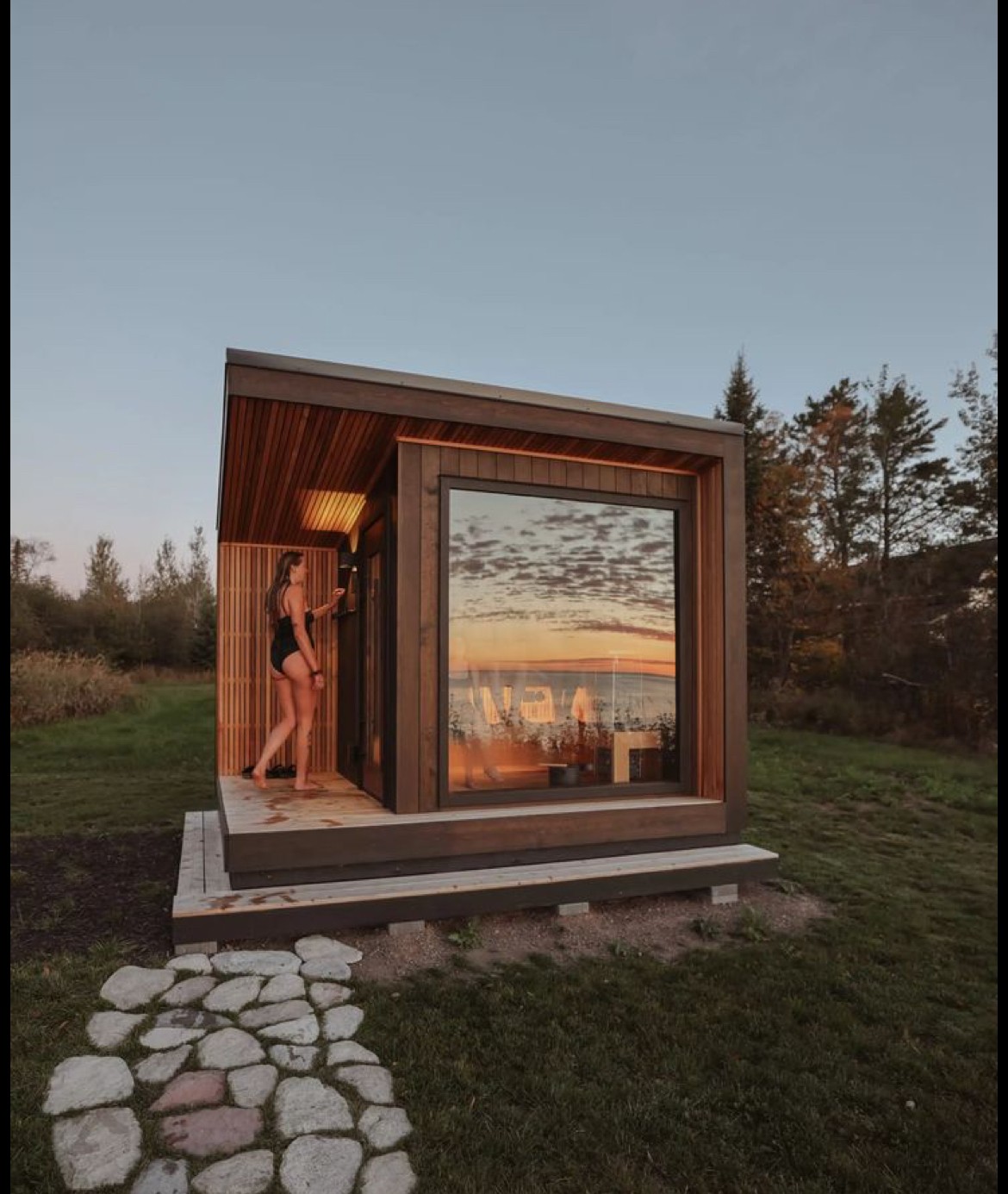 A smiling woman with her arms crossed, standing against a dark green background. She has long, dark hair.