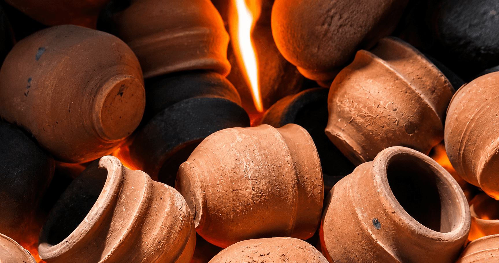Poteries en terre cuite en cours de cuisson entourées de flammes et de pierres noires