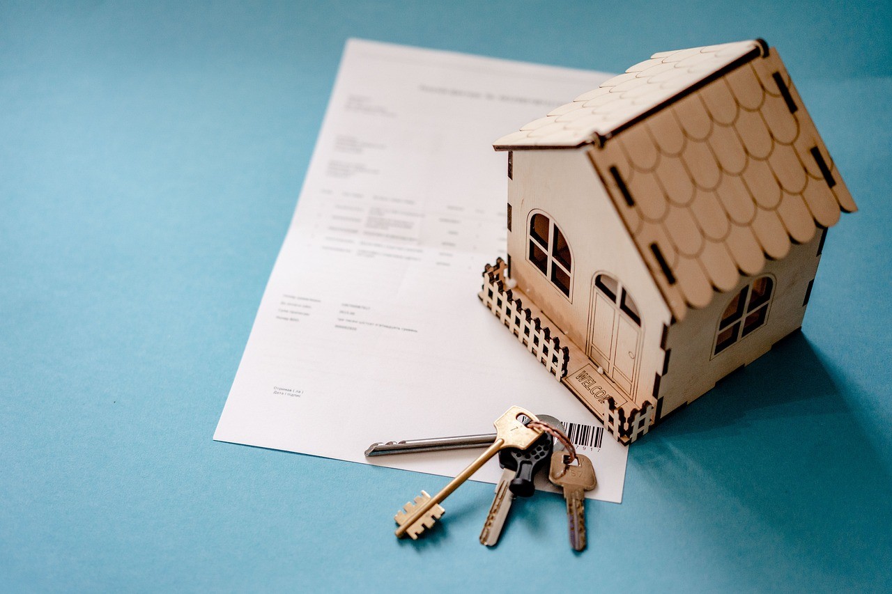 A small wooden house with keys beside it on top of a rental agreement document.