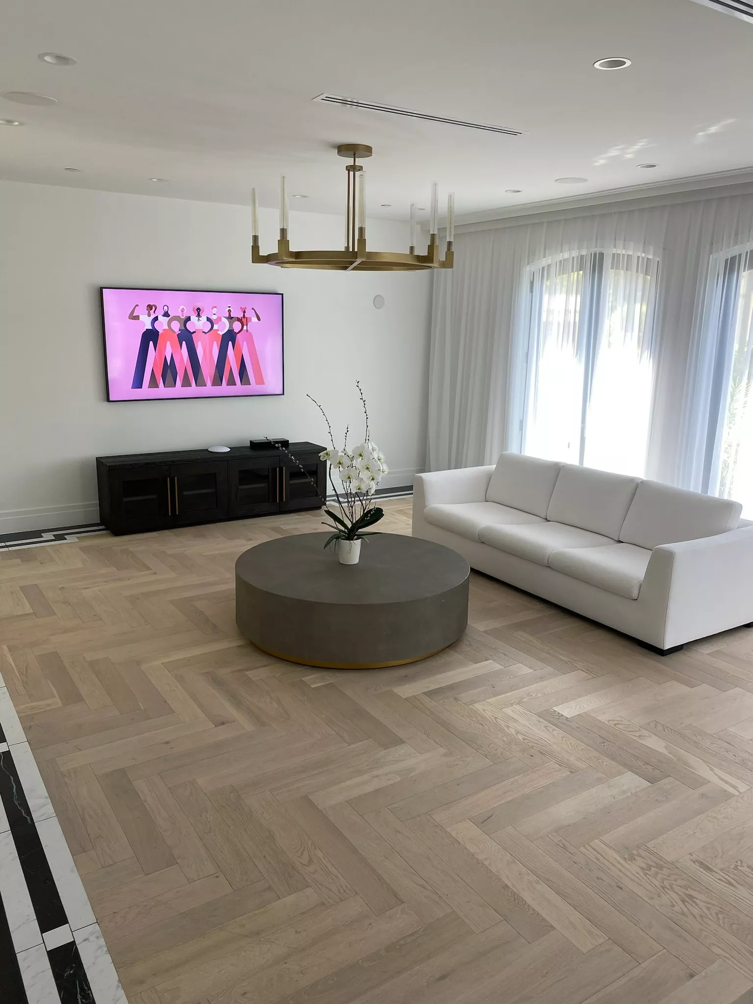 A man and woman sit on beige chairs in a modern room with a red paneled wall. A red pendant light hangs above a wooden coffee table between them.