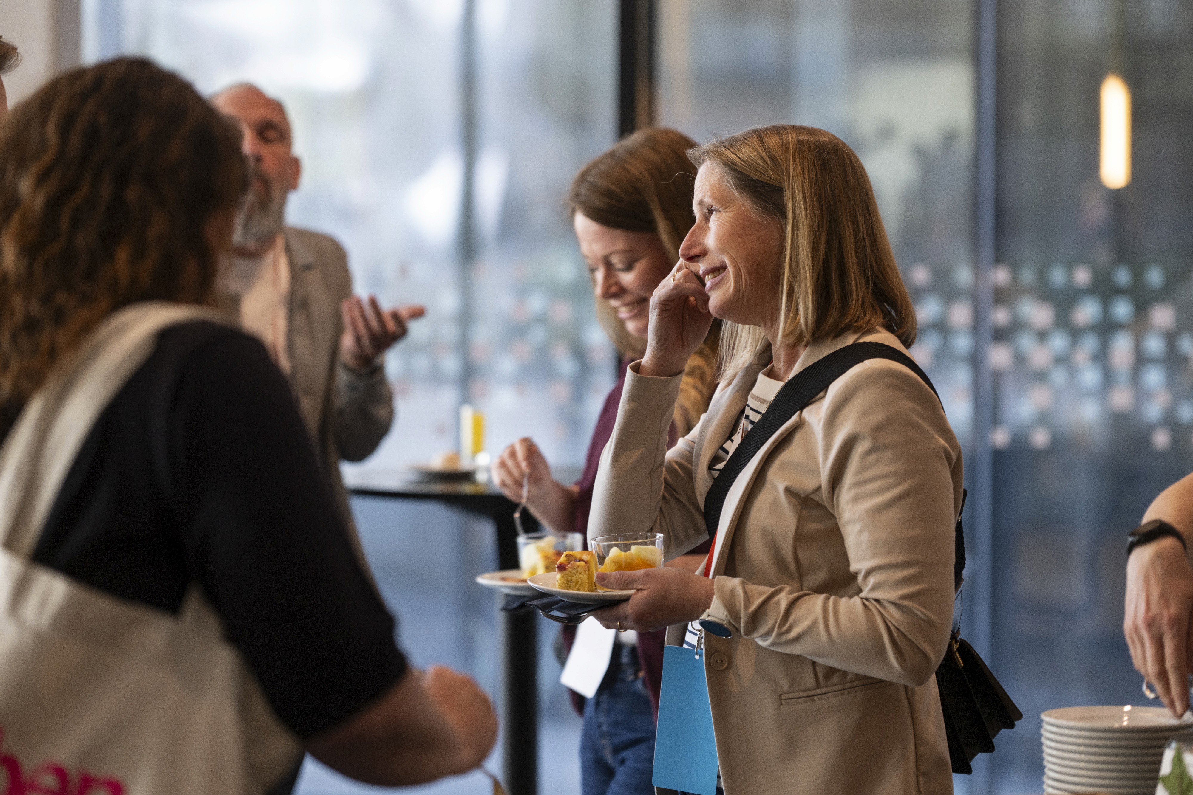 A group of people engaging in conversation at an event, one holding a plate of food.