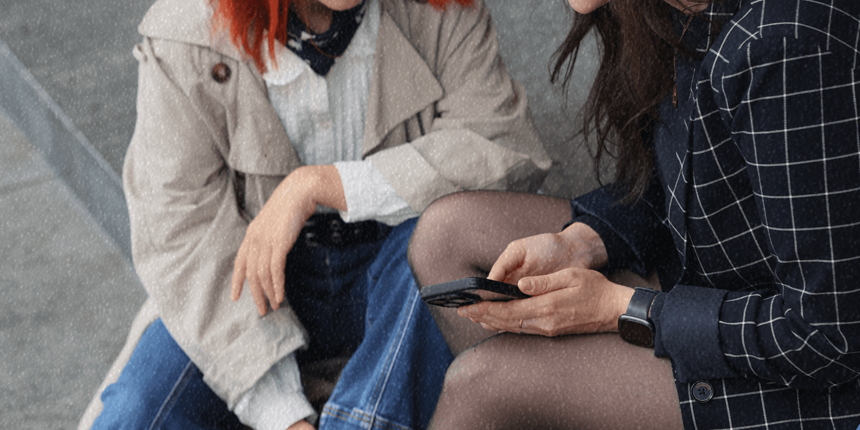 Image is a close up showing two women's upper bodies in work attire, holding a phone.