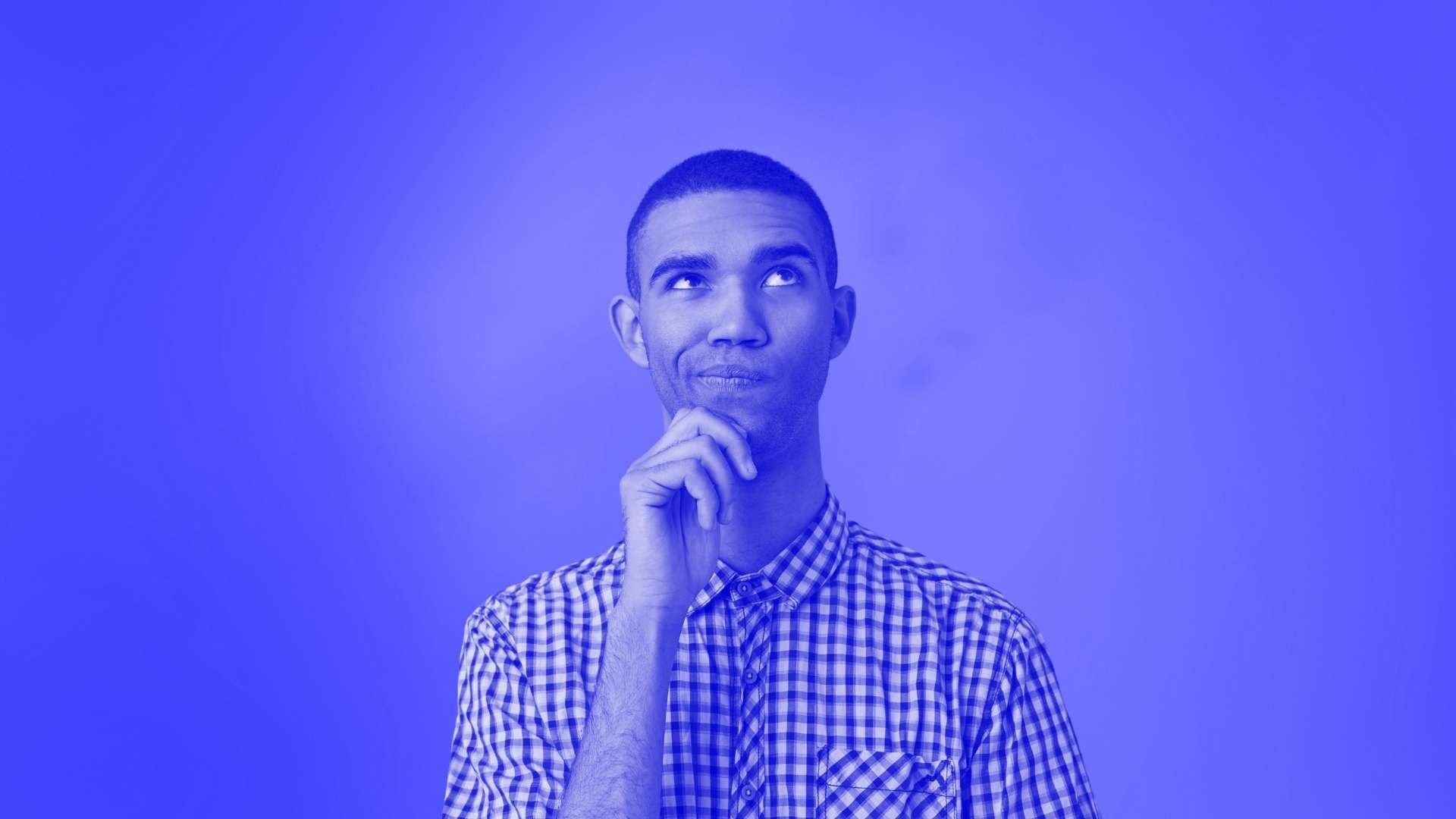 A man wearing a checked shirt with his hand on his chin thinking