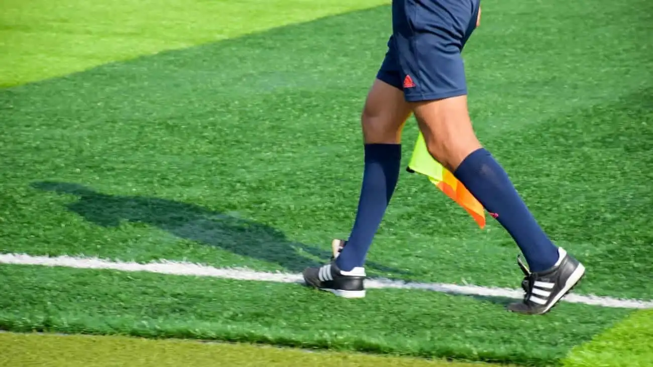 Close-up of a football referee with linesman's flag on the green pitch, symbolising the increase in the number of referees in Bavaria and the positive development in the field of sports officials.