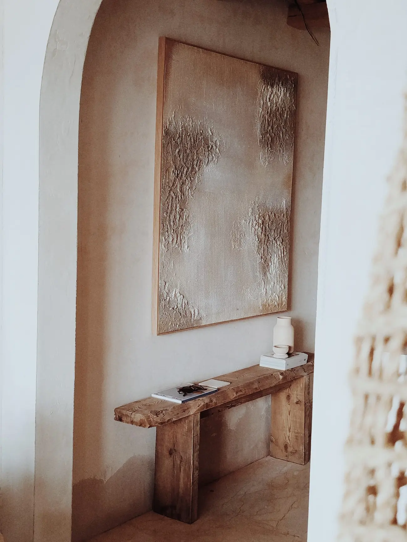 Mediterraner Rundbogen mit Blick auf ein Kunstwerk und rustikale Sitzbank im Referenzprojekt Casa Terra mit massgeschneidertem Interior Design.