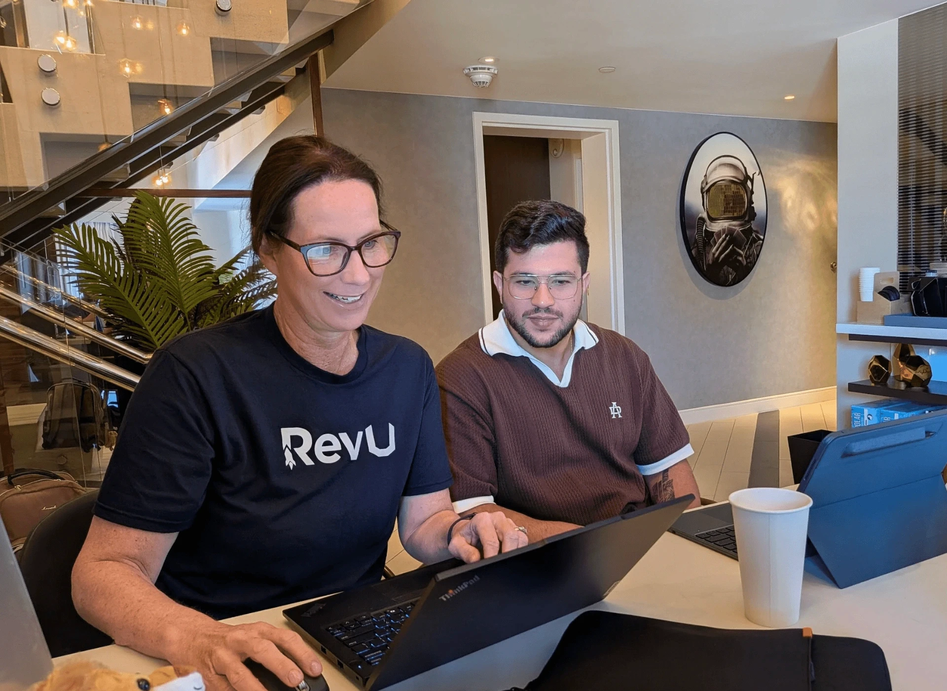 Woman in RevU shirt and man collaborate on laptops for an offerwall.
