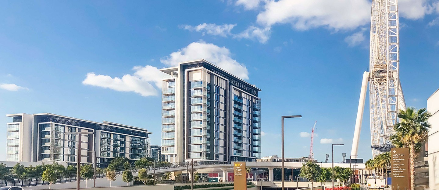 A daytime view of modern apartment buildings on Bluewaters Island in Dubai, with a section of the massive Ain Dubai Ferris wheel visible on the right.