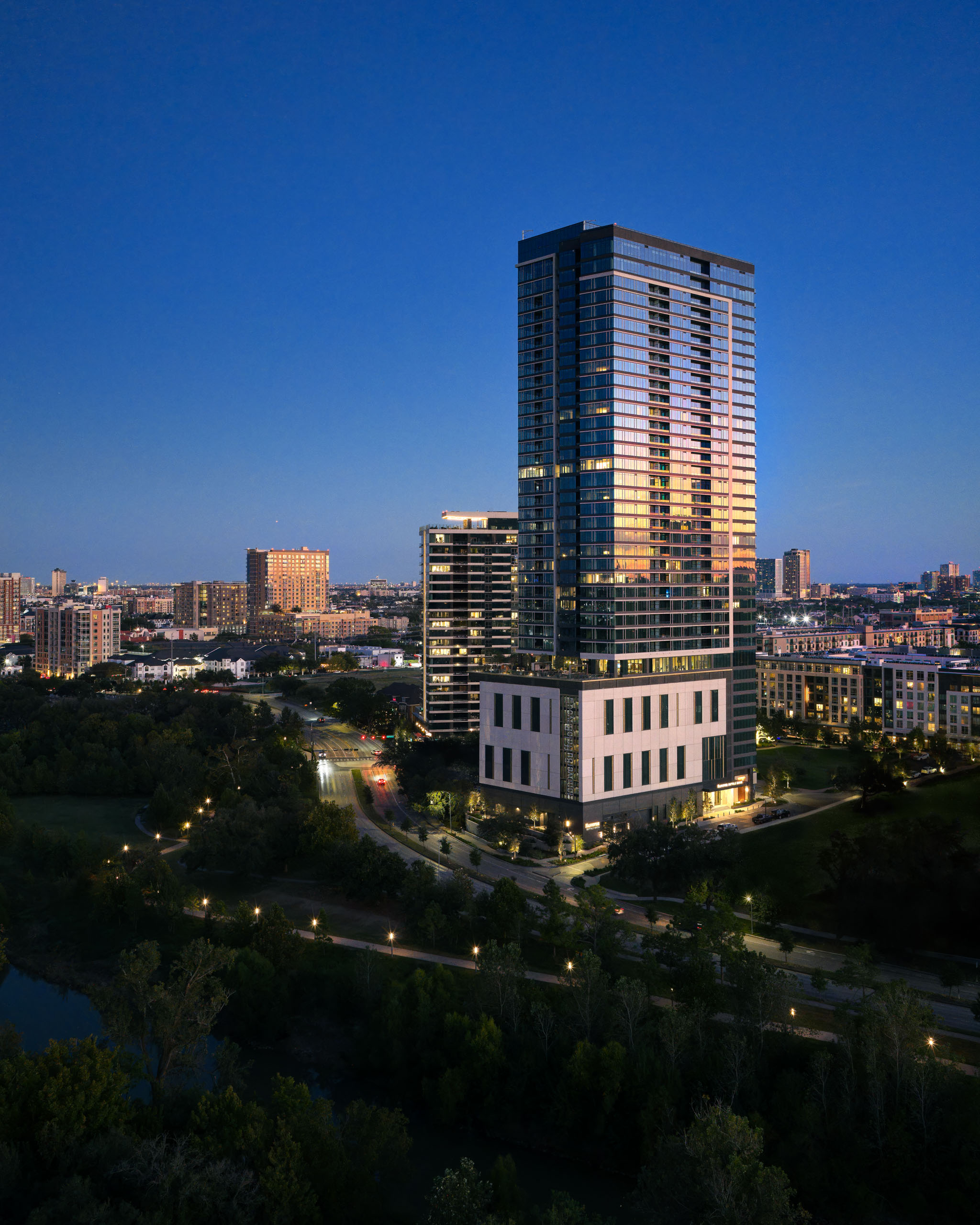 Modern high-rise buildings at twilight with forest and road.