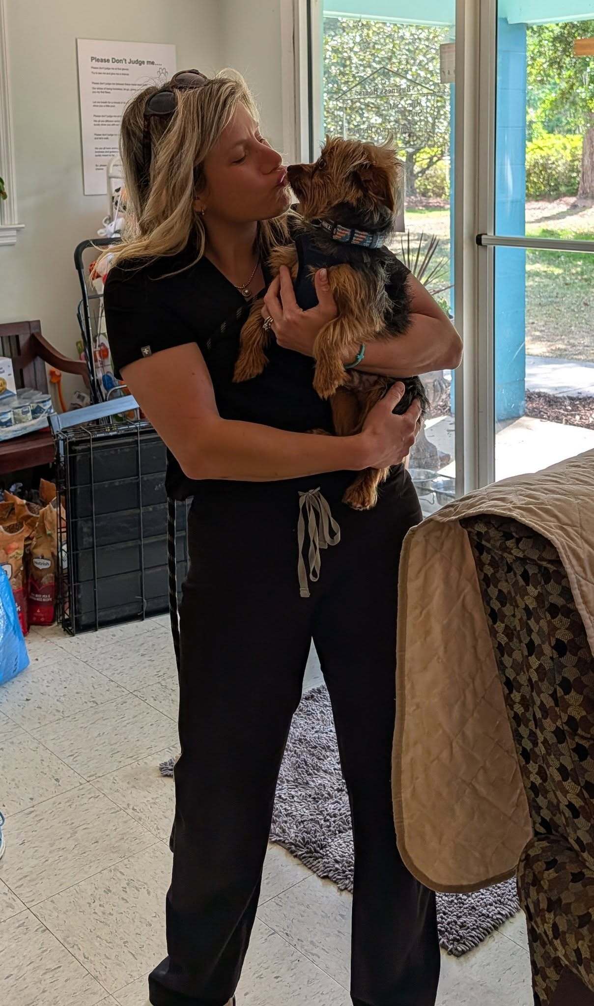 A woman is holding a child in her arms, both smiling, in a bright, cozy interior space.