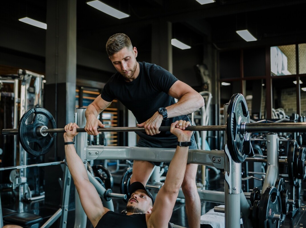 man spotting his friend while he does bench presses at the gym as part of his weight loss training program