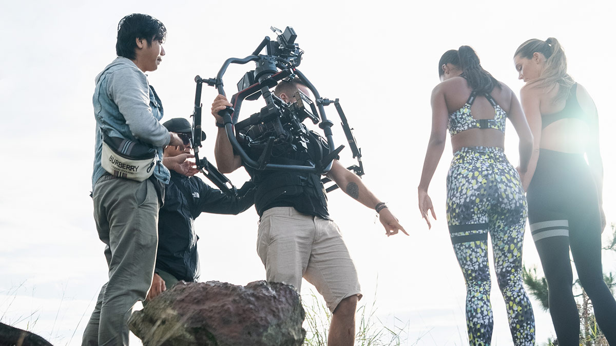We Do Creative film crew and talent on a volcanic highland location in Bali during a commercial activewear campaign, DOP operating a gimbal vest rig with models in foreground