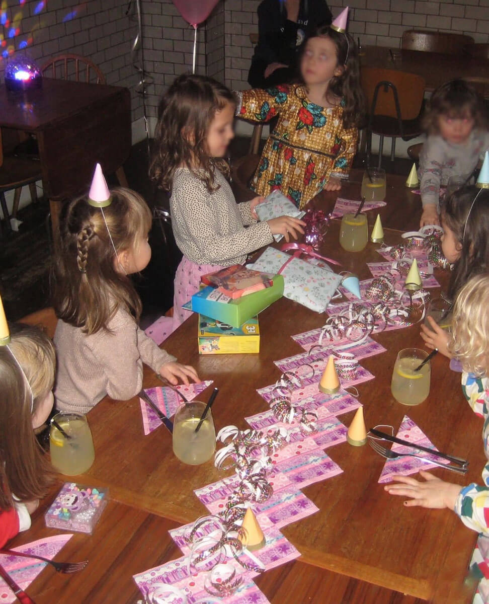 Children gathered around the table while one child unwraps gifts