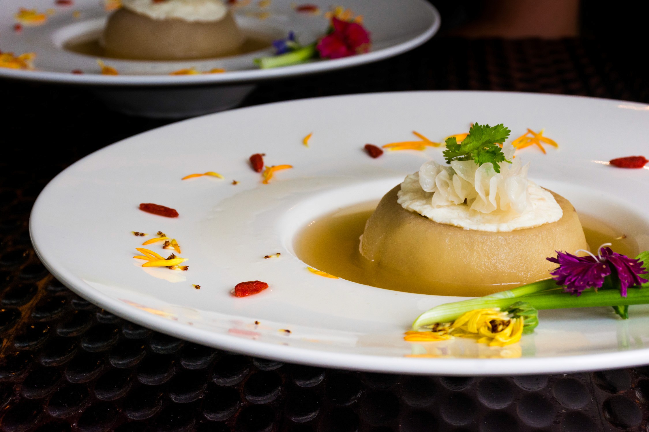 Golden dessert presented on a white plate, garnished with vibrant orange petals under soft, warm lighting.