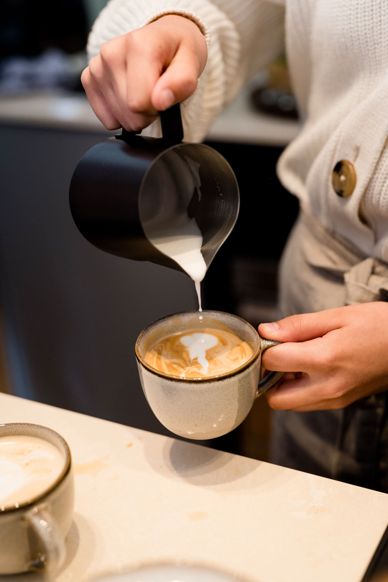 A chilled glass of iced coffee with milk, served with a black straw on a wooden table beside a small white label.