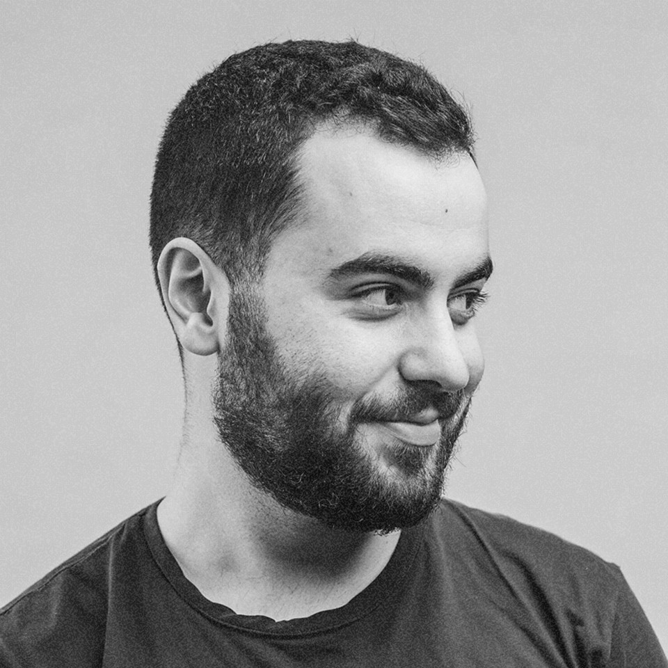 Portrait of a man with short dark hair and a trimmed beard, dressed in a dark shirt, on a simple background.