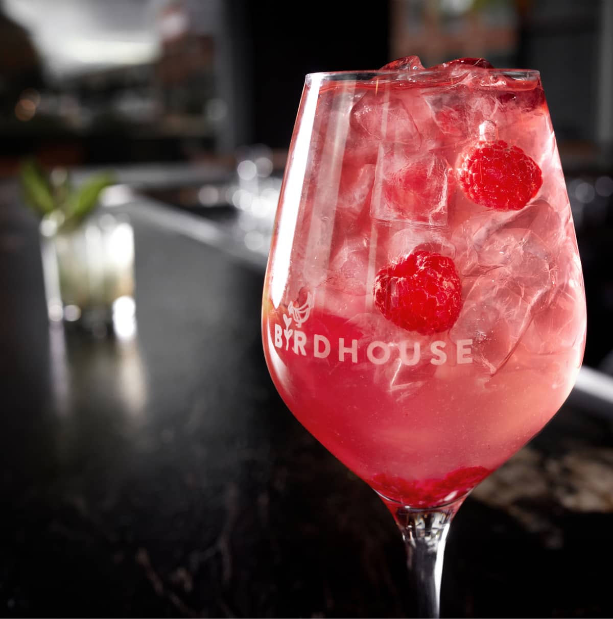 Vue rapprochée d'un cocktail aux framboises dans un verre avec le logo du restaurant Birdhouse