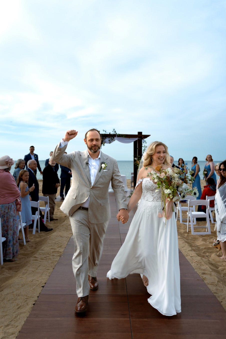 A smiling couple sits on a white blanket in a lush green field.