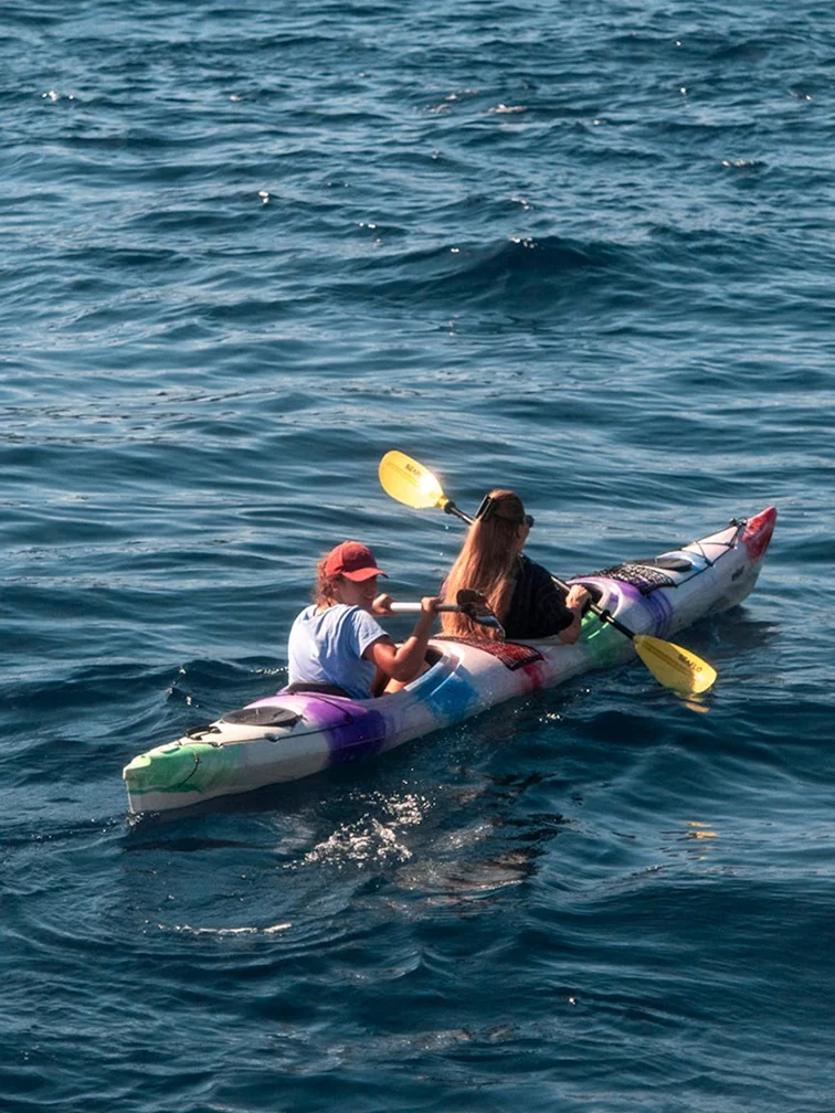 Two guests kayaking together on open ocean water.