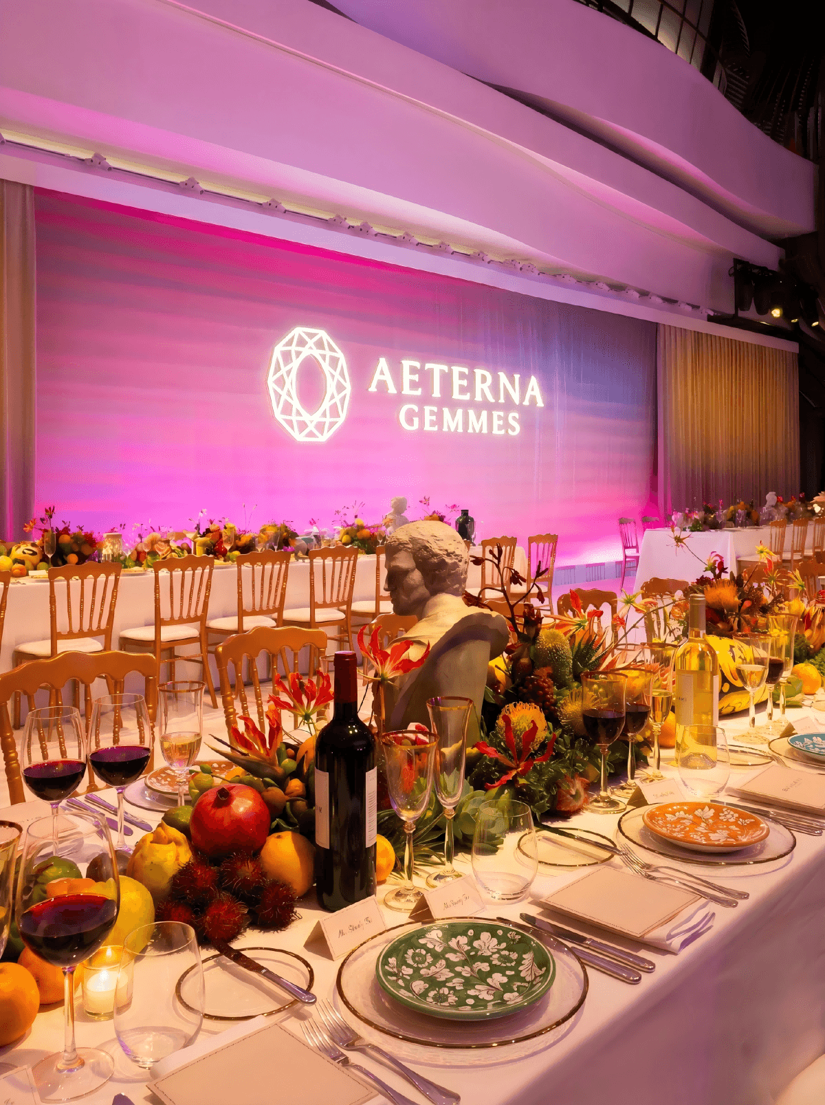 珠寶品牌AETERNA GEMMES於香港舉辦主題長桌晚宴，舞台LED品牌logo搭配豐富水果花藝與紅白酒餐桌佈置，展現高端品牌活動與貴賓款待 AETERNA GEMMES luxury brand gala dinner long table setup in Hong Kong