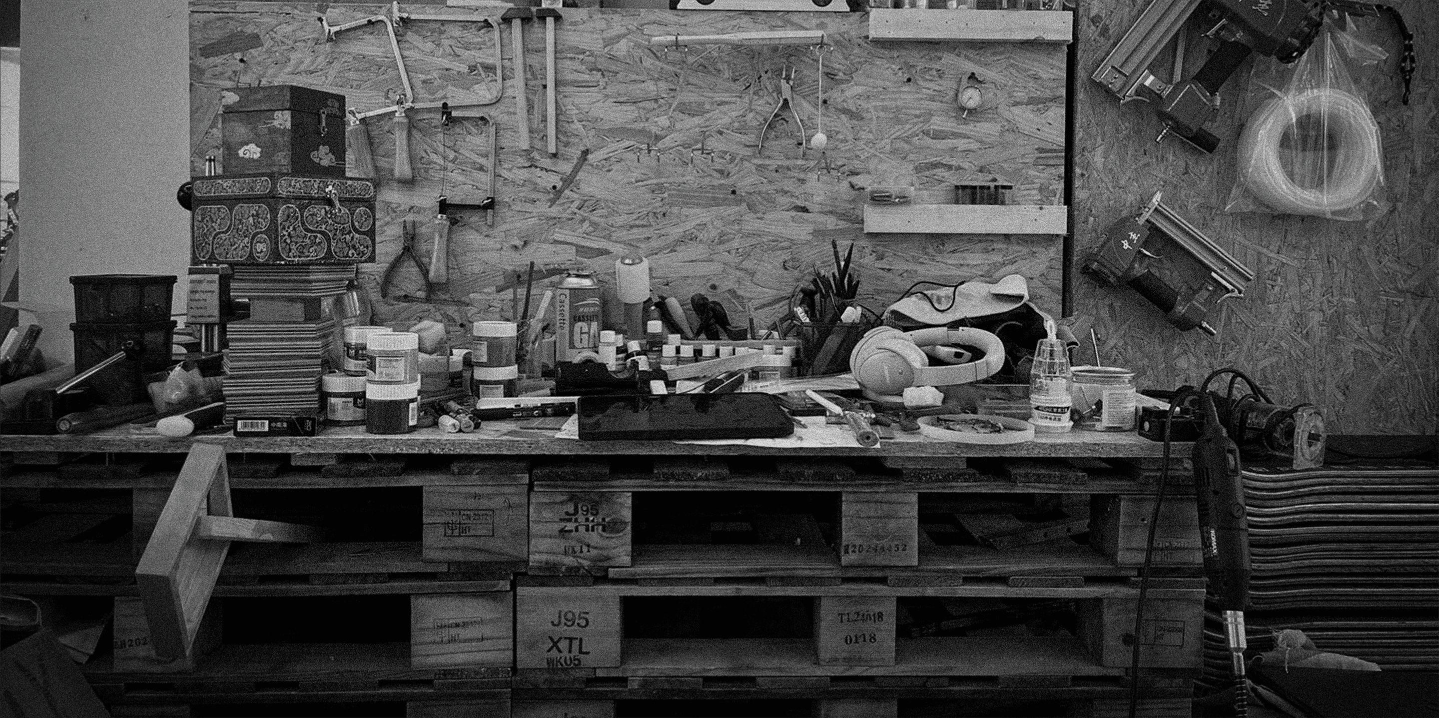 Black and white photo of a cluttered industrial design workbench showing tools, materials, and a headset.
